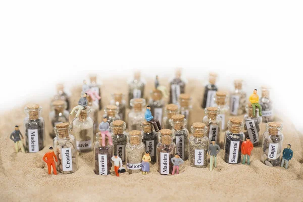 Tubul de testare din sticlă cu nisip din diferite destinații de vacanță de vară. Situat în nisip cu figuri de oameni mici . — Fotografie, imagine de stoc