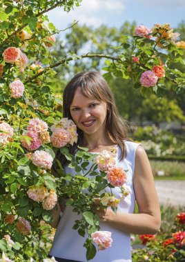 Güller bahçesinde ve gülümseyen mutlu kadın güneşli yaz gününde.