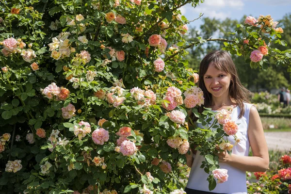 Τριαντάφυλλα κήπο και χαμογελαστή ευτυχισμένη γυναίκα την ηλιόλουστη μέρα του καλοκαιριού. — Φωτογραφία Αρχείου