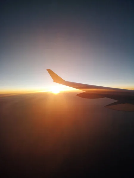 Sunset from a plain. View through the window of an aircraft. Wing of the plane above clouds