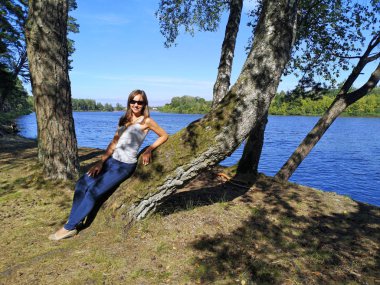 Genç bir kadın nehir kıyısında oturuyor. Güneşli yaz günü.