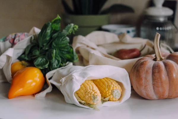Eko tote çanta sonbahar hasat ile. Sarı domates, taze Mısır, kabak ve mutfak masasının üzerinde alışveriş torbaları ile armut