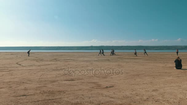 Νέοι άνδρες παίζουν ποδόσφαιρο σε μια ερημική παραλία κοντά σε ένα ποτάμι. — Αρχείο Βίντεο