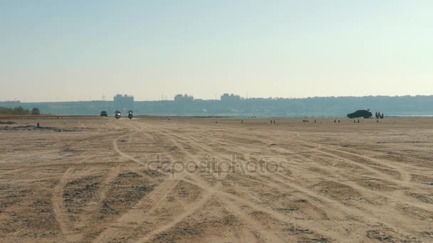 Tres motociclistas cabalgando cerca de la playa de arena en el desierto desde muy lejos. Paseo en bicicleta . — Vídeos de Stock