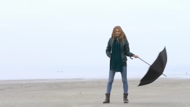 Mooie jonge meisje draaien en te spinnen paraplu en plezier op mistige strand — Stockvideo