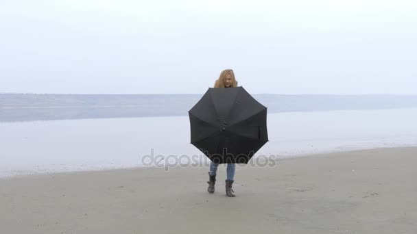 Lány mögött esernyő gyaloglás felé kamera, a homokos strandtól és a nevet. — Stock videók