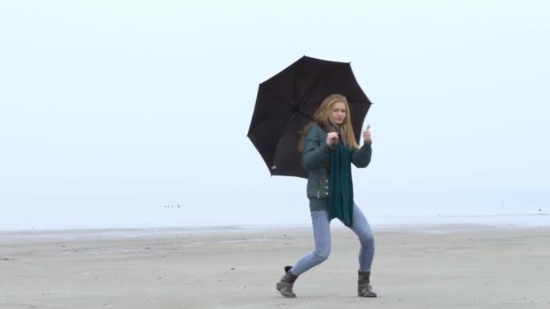 Hezká mladá dívka tančí s deštníkem a baví na mlhavé beach — Stock video