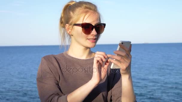Piękna młoda dziewczyna korzysta smartfon w pobliżu morza — Wideo stockowe