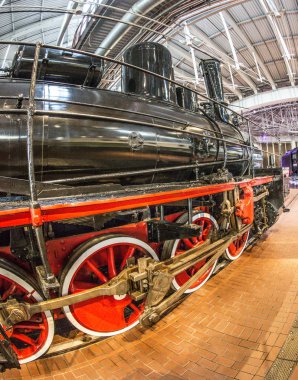 Kırmızı tekerlekleri olan eski siyah bir buhar makinesi ve kırmızı yıldızlı kırmızı bir tampon istasyondaki platformda duruyor.