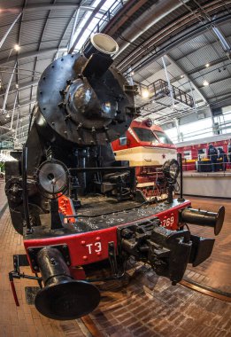 Kırmızı tekerlekleri olan eski siyah bir buhar makinesi ve kırmızı yıldızlı kırmızı bir tampon istasyondaki platformda duruyor.