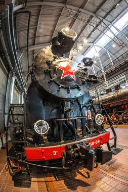 Kırmızı tekerlekleri olan eski siyah bir buhar makinesi ve kırmızı yıldızlı kırmızı bir tampon istasyondaki platformda duruyor.