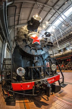 Kırmızı tekerlekleri olan eski siyah bir buhar makinesi ve kırmızı yıldızlı kırmızı bir tampon istasyondaki platformda duruyor.