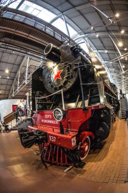 Kırmızı tekerlekleri olan eski siyah bir buhar makinesi ve kırmızı yıldızlı kırmızı bir tampon istasyondaki platformda duruyor.