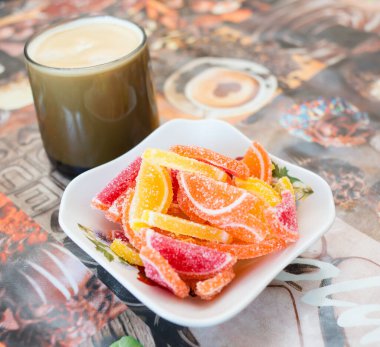 Bir bardak sütlü kahve ve bir vazo renkli marmelat.