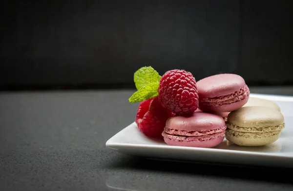 Macaroons rosa com framboesas. Fundo escuro . — Fotografia de Stock