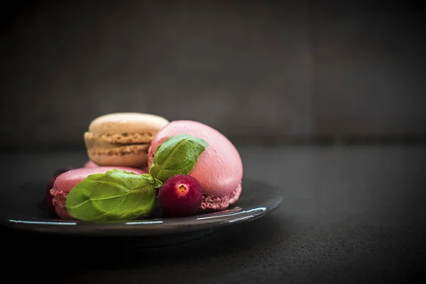 Macaroons doces ou macarons com cranberry e flor. fundo de concreto escuro — Fotografia de Stock