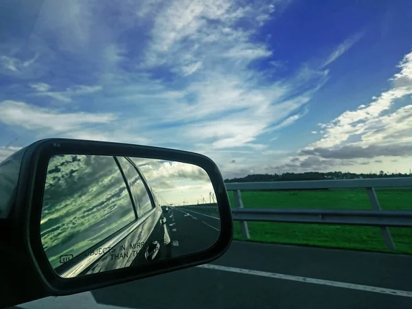 Rear view mirror reflecting road and sky