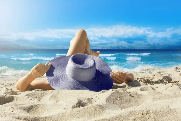 La ragazza con un cappello si siede sulla spiaggia, guardando il mare . — Foto Stock