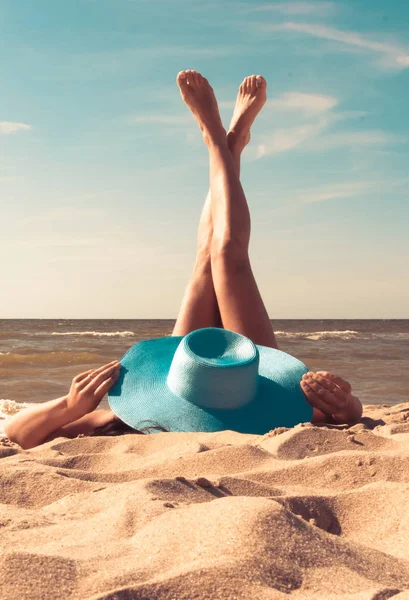 La ragazza con un cappello si siede sulla spiaggia, guardando il mare . — Foto Stock