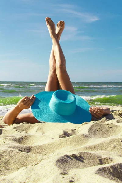 La ragazza con un cappello si siede sulla spiaggia, guardando il mare . — Foto Stock