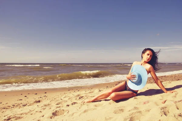 Das Mädchen mit Hut sitzt mit dem Rücken am Strand und blickt auf das Meer. — Stockfoto
