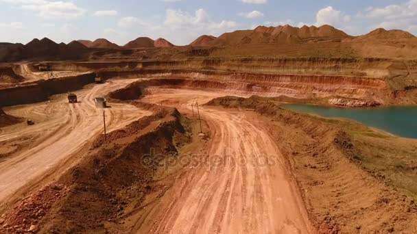 Deux camions à benne se déplacent dans la carrière. Pelles. Extraction de minerai. L'exploitation minière. Bouxite. Panorama. Terre rouge. Lac artificiel azur. Vue depuis le drone . — Video