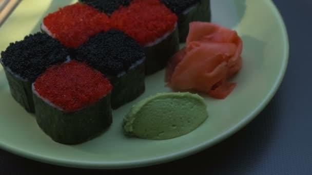 "Cheess "vierkante Sushi broodjes met zalm, komkommer, roomkaas, rode en zwarte tobiko, nori, sushi-rijst. Plaat. Stokjes, gemarineerde gember en wasabi. Close-up. — Stockvideo