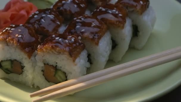 Appetizing incrível "Dragon" rolos de sushi quadrados com enguia, salmão, pepino, nori, arroz sushi, sésamo. Placa. Chopsticks, gengibre marinado e wasabi. Close-up . — Vídeo de Stock