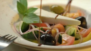 Salatalık, domates, biber, zeytin ve peynir ile Yunan salatası balsamik sirke ile dekore edilmiştir. Ağır çekim.