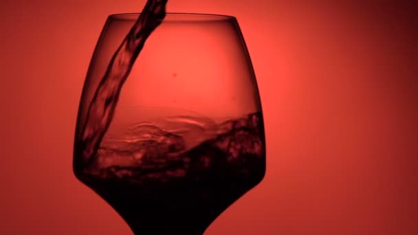 Copa llena de vino sobre fondo rojo. Movimiento lento . — Vídeos de Stock