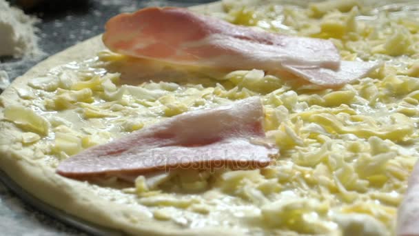 Cooking pizza. Grated cheese and slices of ham on the raw pizza. Close-up. Slow motion. — Stock Video