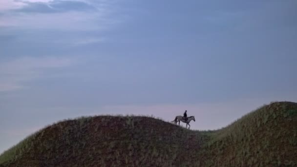 The lonely shepherd on a white horse rides through the green hills against the sky. — Stock Video