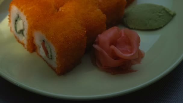 Rollo de sushi, rollos de california en un plato con palillos, jengibre marinado y wasabi. Primer plano. Haz de luz . — Vídeo de stock