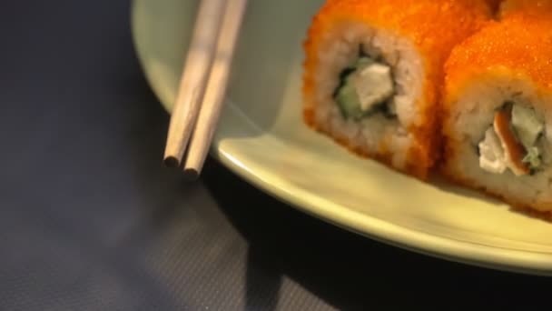 Sushi rulle, Kalifornien rullar på en tallrik med ätpinnar, marinerad ingefära och wasabi. Närbild. Ljusstrålen. — Stockvideo