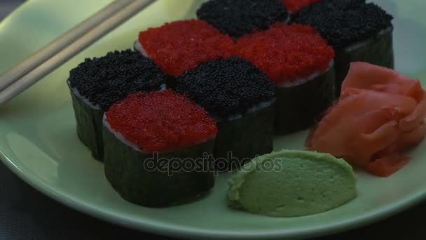 "Cheess" square sushi rolls with salmon, cucumber, cream cheese, red and black tobiko, nori, sushi-rice. Plate. Chopsticks, marinated ginger and wasabi. Close-up. — Stock Video