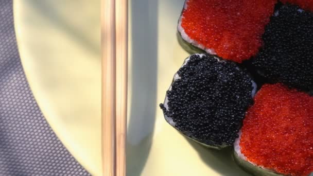 "Cheess" square sushi rolls with salmon, cucumber, cream cheese, red and black tobiko, nori, sushi-rice. Plate. Chopsticks, marinated ginger and wasabi. Close-up. — Stock Video