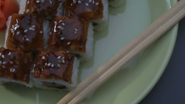 Аппетитные квадратные суши "Дракон" с угрем, лососем, огурцом, нори, суши-рисом, кунжутом. Тарелка. Палочки, маринованный имбирь и васаби. Крупный план . — стоковое видео