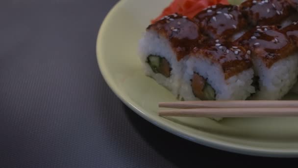 Appetizing incrível "Dragon" rolos de sushi quadrados com enguia, salmão, pepino, nori, arroz sushi, sésamo. Placa. Chopsticks, gengibre marinado e wasabi. Close-up . — Vídeo de Stock