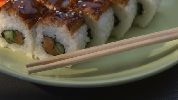 Ορεκτικές καταπληκτική «Δράκος» τετράγωνο σούσι κυλίνδρους με Χέλι, σολομός, αγγούρι, nori, ρύζι σούσι, σουσάμι. Πλάκα. Τσοπ στικς, τουρσί τζίντζερ και wasabi. Γκρο πλαν. — Αρχείο Βίντεο