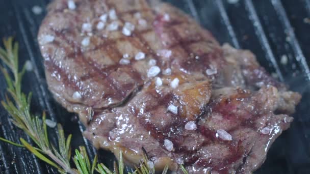 Le steak de boeuf sur le gril est saupoudré de gros sel de mer et de poivre noir. Mouvement lent . — Video