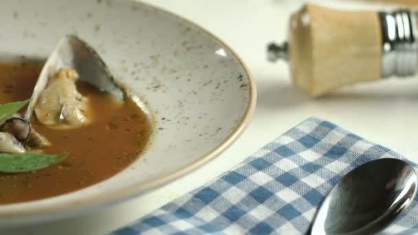 Sopa de tomate con mariscos decorados con hojas de albahaca y tomates cherry en plato blanco sobre la mesa. La mano añade la ostra. cámara lenta . — Vídeos de Stock