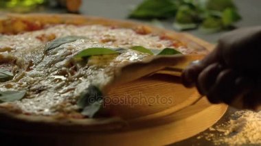 Dilim eritilmiş peynir ile yüksek Delicious Pizza kaldırdı ve fesleğen yaprağı üzerinde ahşap kesme kurulunu, ağır çekim.