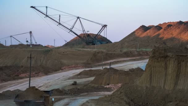 Широкий снимок действующей шахты с погрузкой руды на задний план экскаваторами в сумерках. Задний вид проезжающего самосвала. Бокситовый карьер . — стоковое видео