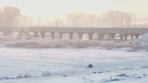 Amplio tiro de puente de carretera que cruza el río congelado en invierno en el helado amanecer de niebla . — Vídeos de Stock