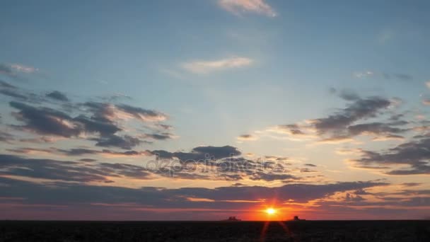 Zeitraffer der Abenddämmerung mit Sonnenuntergang und fließenden bunten Wolken über dem Feld, das von Traktoren bearbeitet wird. — Stockvideo