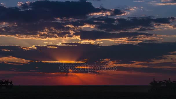 Temps écoulé depuis le crépuscule avec le coucher du soleil et les nuages colorés qui coulent au-dessus du champ cultivés par des tracteurs . — Video