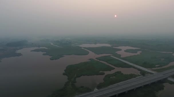 Vista aérea. El pintoresco paisaje con río, puente de carretera, árboles y campo con sol increíble. Niebla matutina . — Vídeos de Stock