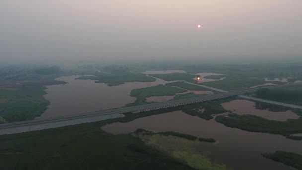 Вид с воздуха. Живописный пейзаж с рекой, автодорожным мостом, деревьями и полем с Невероятным солнцем. Утренний туман . — стоковое видео