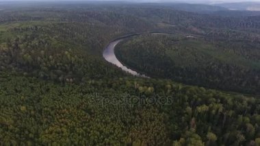 Bulutların arasından nehir ve güneş ışınları ile iğne yapraklı orman kaplı dağları'nın hava atış.