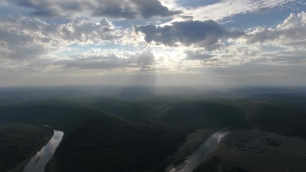 Tiro aéreo de montanhas cobertas com floresta de coníferas com rio e raios de sol através das nuvens . — Vídeo de Stock